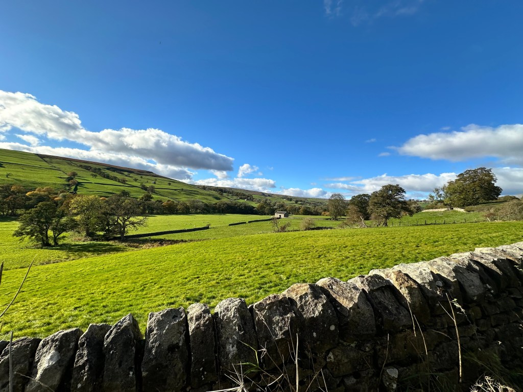 A vivid blue sky with fluffy clouds drifting over rolling green hills.